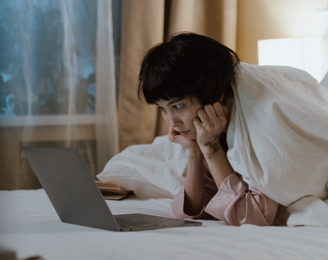 Girl alone in bed with a duvet over her watching her laptop